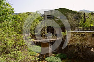 Footbridge over weedy riverway in deserted 1970s` factory