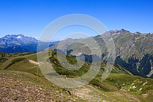 Footpath in alpine meadows and rocky mountains covered with snow