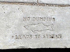 A footpath edging sign by a drain stating `No Dumping-Leads to Stream`