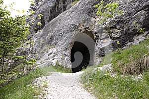 Footpath leading to entrance to the cave in Jura mountains. Black hollow in rock. Mountain tunnel hiking trail, cave enter of dark