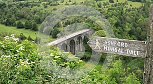 Footpath sign to Ashford Monsal Dale in front of the panoramic landscape looking down to the Monsal trail viaduct in Derbyshire