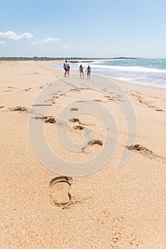 Footprints along the sand coast, a group of four people are hanging out in the beach, the ocean has just a single wave