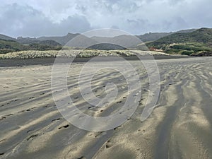 Footprints on a black sand at Bethells Beach, New Zealand