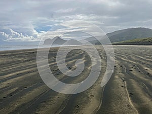Footprints on a black sand at Bethells Beach, New Zealand