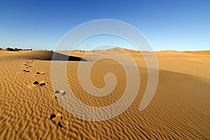 Footprints on desert sand dunes with blue sky