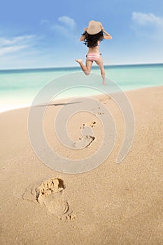 Footprints and excited woman running at beach