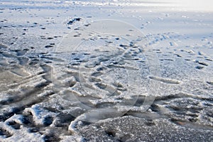 Footprints on a frozen lake with snow surface and thin ice