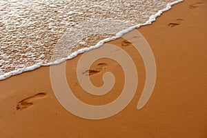 Footprints at golden sand, footsteps. Tropical beach with sea sand on summer vacation.