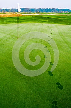 Footprints on golf grass near flag in dew