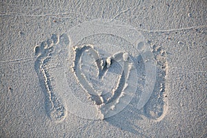 Footprints of the groom and the bride`s feet and a painted heart on the sand of the beach.