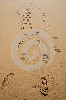 Footprints of hiking boots on the sand of a beach.