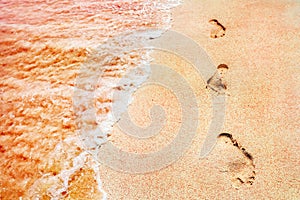 Footprints of the people on a golden pink sand on the sea coast. Soft waves of pink color. Marine creative background close up