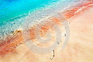 Footprints of the people on a golden pink sand on the sea coast. Soft waves of pink, red and blue color. Multicolores sea water.