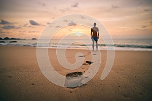 Footprints in sand against silhouette of person