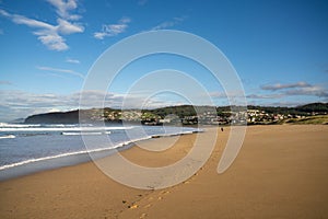 Footprints in the sand on a beautiful beach and woman walking in the distance