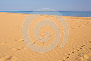 Footprints in the sand at sunset. Beautiful sandy tropical beach with sea waves. Footsteps on the shore.