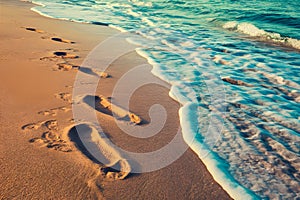 Footprints on sandy beach being washed away, transient imprints