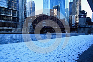 Footprints on snow covered riverwalk across a frozen and ice chunk filled Chicago River