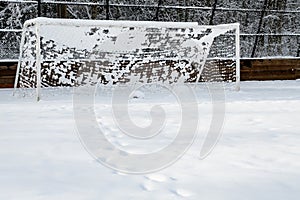 Footprints in the snow leading up to the goal on a snow covered soccer field, with a forest background