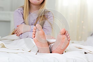 Foots of child girl is sitting in the bed