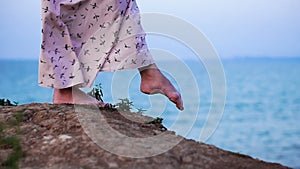 Foots of girl in Light Dress Walking at the Enge of Cliff above the Sea at Sunrise time