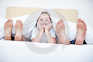 Footsie footsie. Fun shot of a child liying at the end of a bed between her parents feet.