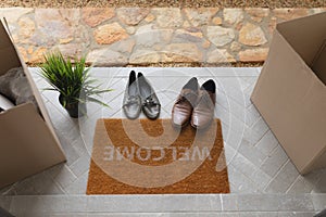 Footwear, cardboard boxes and plant near welcome doormat