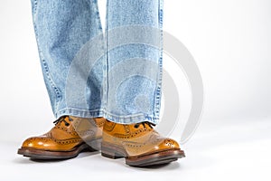 Footwear Concept. Closeup Front View of Mens Legs in Brown Oxford Brogue Shoes. Posing in Blue Jeans Against White