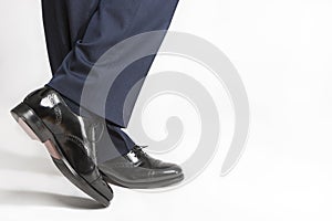 Footwear Concept: Closeup of Stylish Black Shiny Male Semi-Brogue On Crossed Legs Against White