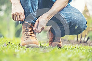 Footwear concept.Handsome man wear jeans knelt down to do up his shoelaces. Preparing before go to party. Brown boots on green