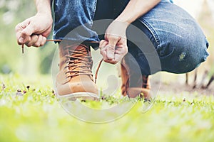Footwear concept.Handsome man wear jeans knelt down to do up his shoelaces. Preparing before go to party. Brown boots on green