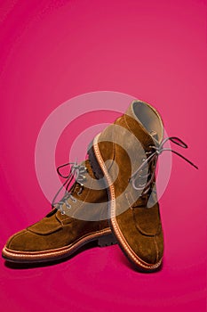 Footwear Concepts. Pair of Tan Brown Suede Split Toe High Boots Closeup With Rubber Sole Placed on One Another Over Pink Red