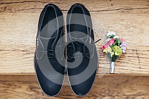 Footwear of the groom lies on the wooden floor and next to the buttonhole