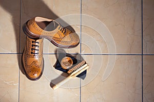Footwear Ideas. Pair of Full Broggued Tan Leather Oxfords Broggued Shoes With Cleaning Brush Set Against Brown Floor Tiles