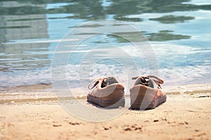 Footwear on the sand by the water of the lake. Shoes on the beach by the sea