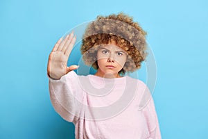 Forbidden prohibited serious caucasian young woman with curly hair, showing with palm hand stop sign gesture isolated in