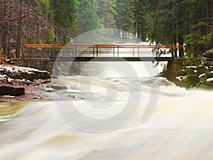 Force of Nature. Huge stream of rushing water masses below small footbridge. High cascade in forest.