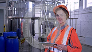 Forceful woman at factory, portrait of engineer female into hard hat and coveralls with computer tablet making