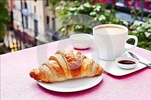 In the foreground is a croissant with a cup of coffee