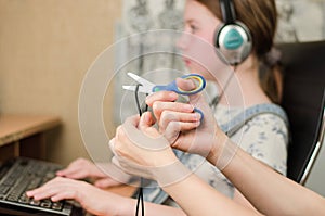 In the foreground, female hands are cutting the headphone cord with scissors, in the background is a girl in headphones