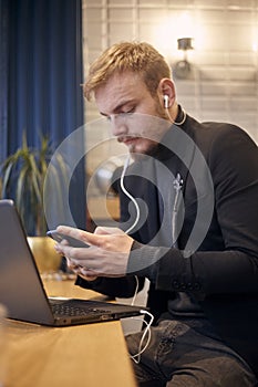 Foreground focus on hand and smart phone, man is out of focus. one young man, sitting indoors in coffee shop and using his smart-