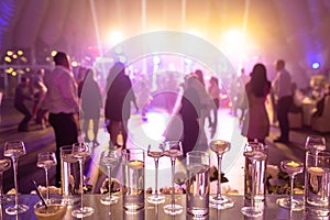Foreground focus vases on glass table with dancing people at wedding