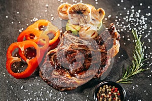 In the foreground, a juicy meat steak is ready on a dark metal cutting board, next to a sprig of aromatic rosemary, a black jar of