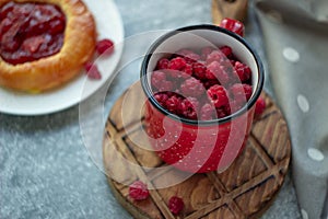 In the foreground is a red mug with garden raspberries, in the background a cheesecake with berry filling, light background, defoc