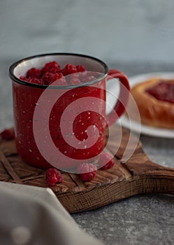 In the foreground is a red mug with garden raspberries, in the background a cheesecake with berry filling, light background, defoc