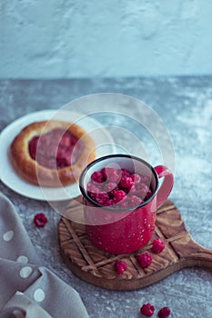 In the foreground is a red mug with garden raspberries, in the background a cheesecake with berry filling, light background, defoc