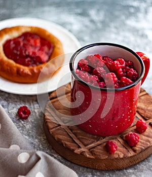 In the foreground is a red mug with garden raspberries, in the background a cheesecake with berry filling, light background, defoc