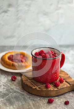 In the foreground is a red mug with garden raspberries, in the background a cheesecake with berry filling, light background, defoc