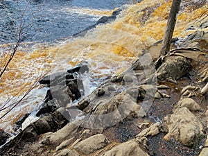 In the foreground, a rock with trees is visible, then a foaming mountain river