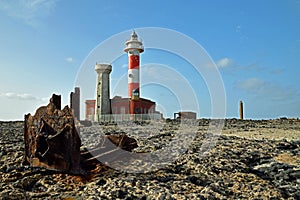 Toston lighthouse Faro de Toston in Fuerteventura with rusty ship wreck in foreground on rocks